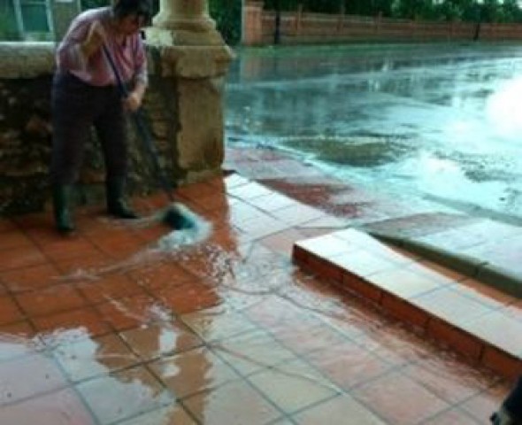 Unas mujeres, achicando agua con cepillos de barrer de la ermita del Loreto, donde está la Oficina de Turismo