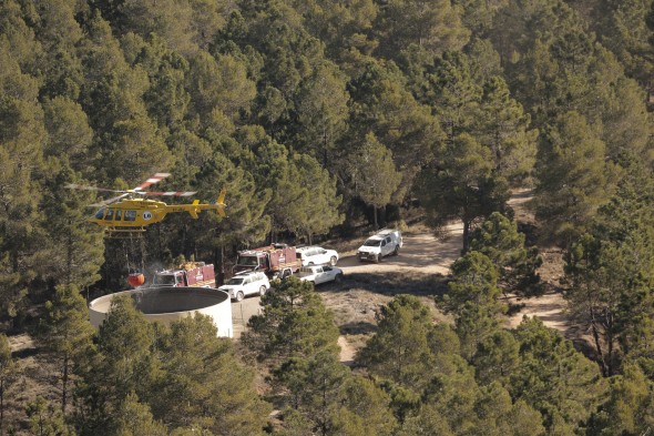 Un helicóptero carga agua junto a dotaciones de bomberos en San Agustín